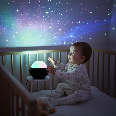 Depuis son lit, le bébé observe les lumières de la veilleuse à projection de l’espace.